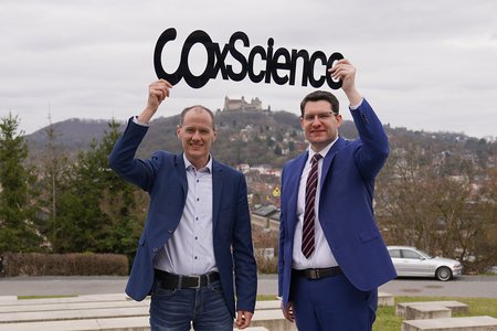Zewi Männer halten ein Schild hoch. Darauf steht: COXScience.
