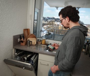 Ein junger Mann steht mit seinem Handy in der Hand in der Küche.