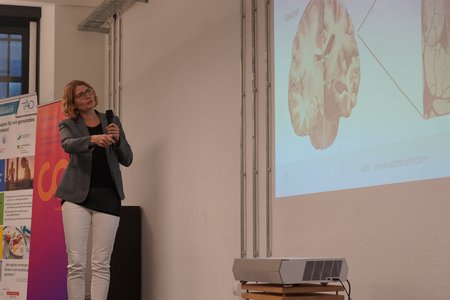 Eine Frau zeigt auf das Bild eines Gehirns an der Wand.