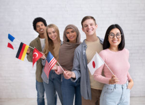 Studierende aus Frankreich, Deutschland, Türkei, USA und Japan stehen nebeneinander, halten Flaggen ihrer Heimatländer in der Hand und lächeln.