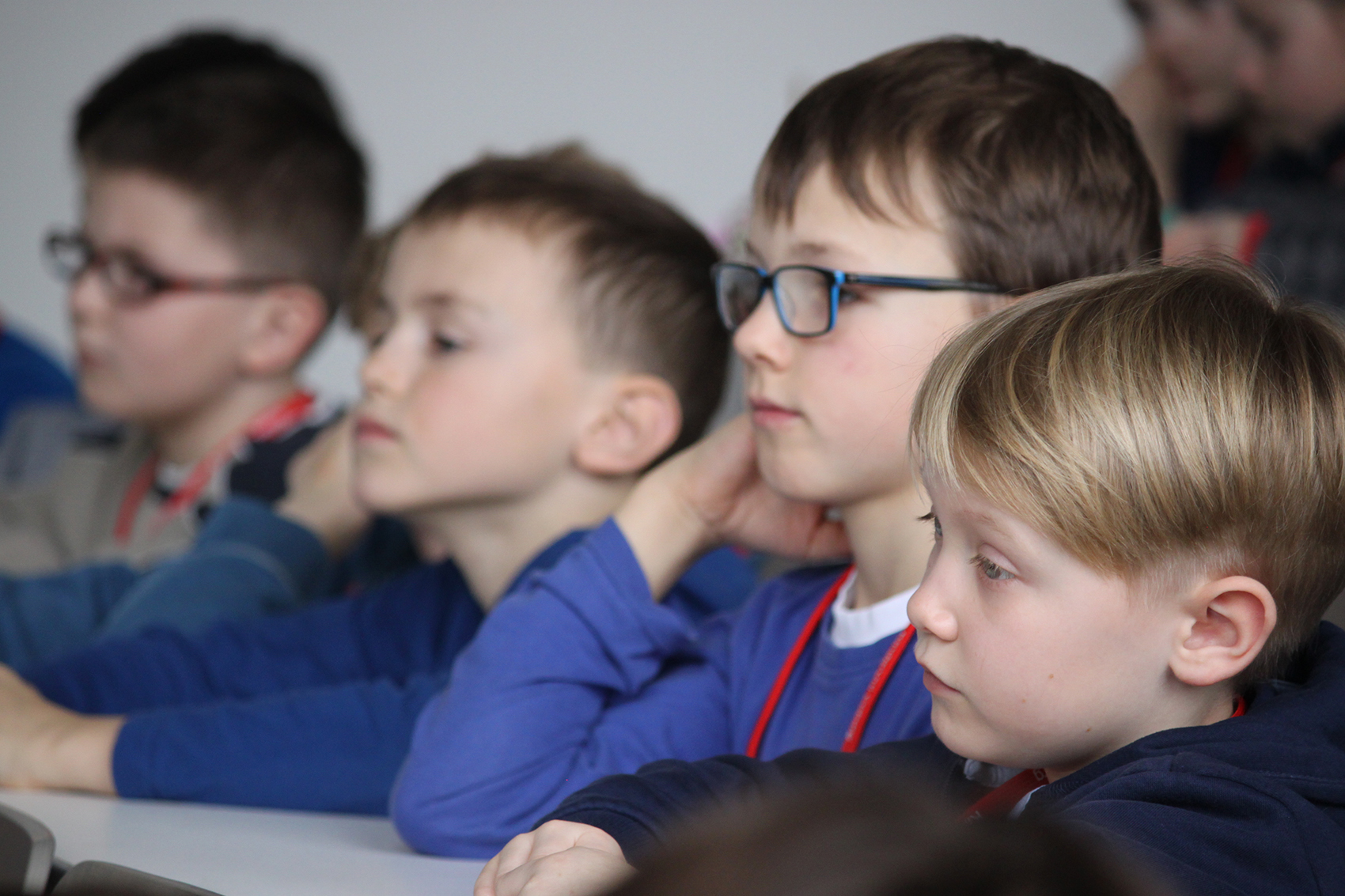 Eine Gruppe junger Jungen in blauen Hemden und mit Brillen sitzt aufmerksam in einem Hörsaal der Hochschule Coburg, ihre Augen sind leicht auf etwas außerhalb des Bildes gerichtet. Die Umgebung lässt vermuten, dass sie in eine Unterrichtsstunde oder Präsentation vertieft sind.