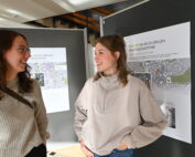 Zwei Frauen stehen vor Schautafeln mit Karten und Informationen zur Hochschule Coburg und unterhalten sich. Sie wirken engagiert und lächeln.