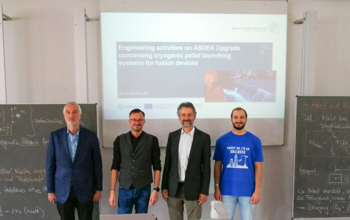 Vier Personen stehen vor einer Präsentationsfolie mit dem Titel „Ingenieuraktivitäten an ASDEX Upgrade zu Startsystemen für kryogene Pellets für Fusionsanlagen“ an der Hochschule Coburg. Neben ihnen stehen zwei Tafeln mit Gleichungen, die ihre wissenschaftliche Arbeit hervorheben.