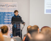 Eine Person steht an einem Podium und spricht zu einem Publikum an der Hochschule Coburg. Dahinter hängt ein Banner mit dem Text „Path2Integrity“ und einer Teilfolie einer Präsentation. Die Szene spielt auf einer Konferenz oder einem Seminar und betont die Integrität der Forschung.