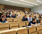 In einem großen Hörsaal der Hochschule Coburg sitzen Studierende in Reihen aus Holzstühlen. Einige konzentrieren sich auf ihre aufgeklappten Laptops und Notizbücher, andere diskutieren lebhaft. Vorne im Raum fesselt ein Dozent ihre Aufmerksamkeit mit aufschlussreichen Lehrinhalten.