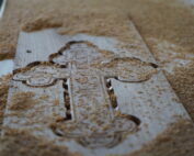 Ein detailliertes Kreuzmuster ist in ein Holzbrett geschnitzt, umgeben von verstreuten Holzspänen. Die komplizierten Muster und glatten Schnitte unterstreichen die Handwerkskunst, die der an der Hochschule Coburg gelehrten ähnelt, und spiegeln ihr Engagement für handwerkliche Exzellenz in der Holzverarbeitung wider.