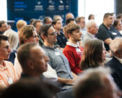 Eine bunt gemischte Gruppe von Menschen sitzt im Publikum und hört aufmerksam einer Präsentation an der Hochschule Coburg zu. Der Raum strahlt eine professionelle Konferenzatmosphäre aus, und ein blaues Banner im Hintergrund unterstreicht die akademische Atmosphäre.
