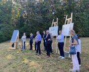 Eine Gruppe von Mitarbeitern der Hochschule Coburg steht im Freien auf einer Wiese neben einer Solarpanel-Ausstellung und großen Informationsplakaten auf Staffeleien. Im Hintergrund sind hohe Bäume zu sehen. Einige beobachten die Präsentation, während andere Mitarbeiter der Hochschule Coburg an der Diskussion teilnehmen.