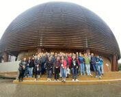 Eine große Gruppe von Menschen steht auf den Stufen vor einem runden, kuppelförmigen Holzgebäude der Hochschule Coburg. Alle sind leger gekleidet und lächeln in die Kamera. Sie versammeln sich unter einem bedeckten Himmel.