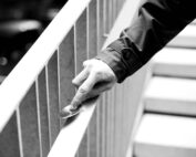 Ein Schwarzweißbild zeigt eine Hand in einem dunklen Ärmel, die beim Treppensteigen an der Hochschule Coburg einen Löffel an einem Metallgeländer entlang schiebt. Der Fokus bleibt auf der Hand und dem Löffel, was ein Gefühl introspektiver Bewegung hervorruft.