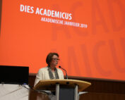 Eine Person steht am Podium und hält eine Rede während der Dies Academicus-Veranstaltung an der Hochschule Coburg. Hinter ihr ist auf einer großen roten Leinwand „AKADEMISCHE JAHRFEIER 2019“ zu sehen.