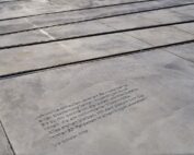 In den Beton neben den Straßenbahnschienen ist ein deutsches Zitat eingraviert, das auf das Warten auf ein Signal zum sicheren Überqueren der Straße hinweist. Es wird Lilo Gunter zugeschrieben (2008). Der Bereich nahe der Hochschule Coburg ist in Sonnenlicht getaucht, was die Sichtbarkeit dieser nachdenklichen Erinnerung erhöht.