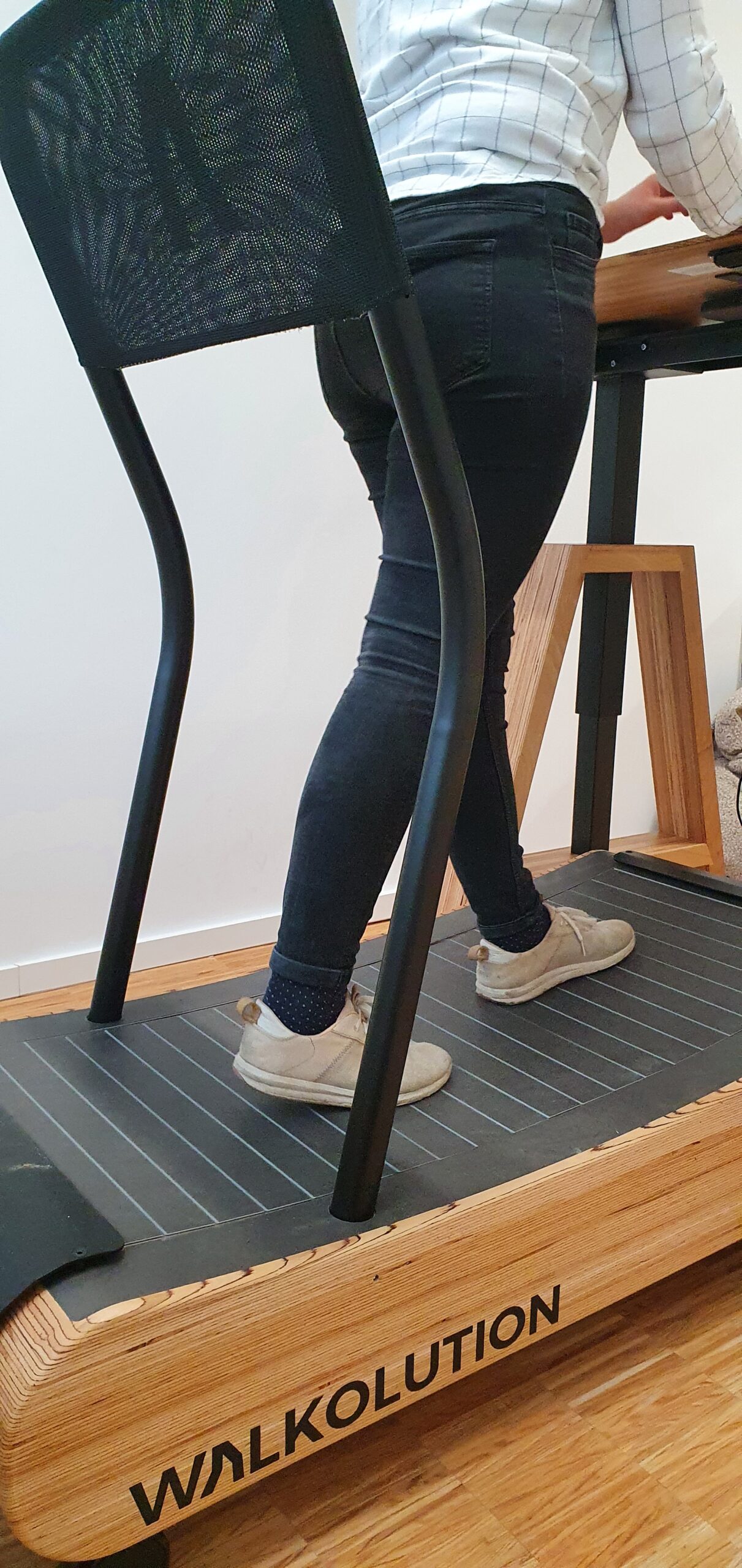 Eine Person an einem Stehpult, stolz in kariertem Hemd, dunkler Jeans und hellen Schuhen, schreitet auf einem Laufband „WALKOLUTION“ umher. Dieser innovative Ansatz spiegelt den dynamischen Geist des Engagements der Hochschule Coburg für Gesundheit und Produktivität wider.