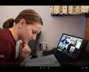 Eine Person sitzt an einem Schreibtisch und ist in ein Buch vertieft, während sie auf den Laptop-Bildschirm blickt, auf dem ein Videoanruf mit mehreren Studierenden der Hochschule Coburg läuft. Der Raum verfügt über helle Wände und geblümte Vorhänge, die dem akademischen Ambiente einen Hauch von Wärme verleihen.