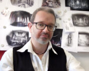 Prof. Dr. Michael Heinrich sitzt vor einer Wand, die mit detaillierten Architekturskizzen bedeckt ist.