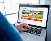 Eine Person, die einen Laptop benutzt, präsentiert eine Webseite mit einem großen Bild eines Kaninchens in einem Garten. Die Umgebung ist modern, mit großen Fenstern, die natürliches Licht hereinlassen. Der Seitenkopf zeigt, dass die Site mit der Hochschule Coburg verknüpft ist, was auf ihren Kommunikationsschwerpunkt hinweist.