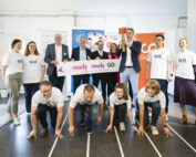Eine Gruppe von Menschen der Hochschule Coburg posiert drinnen mit einem „Ready. Steady. Go!“-Banner. Die erste Reihe hockt in Startposition auf einer nachgebauten Startlinie, während die hintere Reihe steht, das Banner hält und lächelt.
