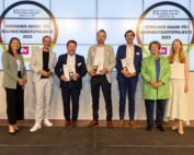 Eine Gruppe von Menschen, darunter Vertreter der Hochschule Coburg, steht lächelnd auf der Bühne, hält Auszeichnungen in den Händen. Hinter ihnen hängt ein mit Logos verziertes Banner mit der Aufschrift „Deutscher Award für Nachhaltigkeitsprojekte 2023“. Die Gruppe besteht aus drei Frauen und vier Männern in Business-Kleidung.