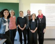 Eine Gruppe von sechs Erwachsenen steht in einem Hörsaal der Hochschule Coburg. Links steht eine grüne Tafel, an die Wand hinter ihnen wird eine Präsentationsfolie projiziert. Sie lächeln und tragen Konferenz-Namensschilder.