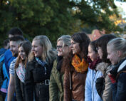 Eine Gruppe junger Erwachsener steht draußen in einer Reihe, lächelt und unterhält sich und verkörpert den lebendigen Geist der Hochschule Coburg. Sie sind in legere Herbstkleidung gekleidet, mit Bäumen und sanftem Abendlicht im Hintergrund.