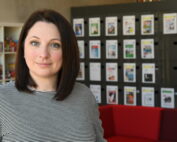 Eine Frau mit schulterlangem, dunklem Haar steht in einem Büroraum der Hochschule Coburg. Sie trägt einen schwarz-weiß gestreiften Pullover. Hinter ihr sind Regale voller Bücher und eine Wand mit verschiedenen Dokumenten. Im Vordergrund ist ein rotes Sofa zu sehen, das der Szene einen Farbtupfer verleiht.