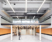 Ein moderner, offen gestalteter Büroraum an der Hochschule Coburg verfügt über ein Zwischengeschoss mit Holzakzenten, Glasgeländern und Industriebeleuchtung. Eine Person geht unter dem Zwischengeschoss im Erdgeschoss entlang.