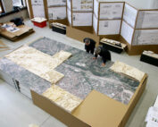 Zwei Personen betrachten ein großes Stadtmodell auf einem Tisch in einem Architekturbüro der Hochschule Coburg. An den umliegenden Wänden hängen Entwürfe und Karten, während auf den Tischen Architekturmodelle und Papiere gestapelt sind, was auf ein laufendes Planungsprojekt schließen lässt.