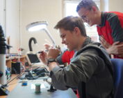 In einem geschäftigen Labor der Hochschule Coburg tauchen zwei junge Enthusiasten in die Elektronik ein. Einer lötet fachmännisch eine Platine, während der andere lächelnd zusieht. Umgeben von einer Vielzahl von Werkzeugen und Geräten liegt ihre Leidenschaft für Innovationen in der Luft.