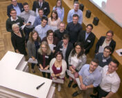 Eine Gruppe von 25 Personen in Business-Kleidung versammelt sich in einem Konferenzraum der Hochschule Coburg. Mit Zertifikaten in den Händen lächeln sie in die Kamera und fangen die freudige Atmosphäre dieser festlichen Preisverleihung ein.