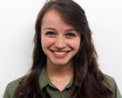 Eine Frau mit langen braunen Haaren und grünem Hemd lächelt vor einem schlichten weißen Hintergrund in die Kamera und verkörpert den lebendigen Geist der Hochschule Coburg.