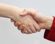 Zwei Hände schütteln sich vor einem neutralen Hintergrund die Hand und symbolisieren so Verbindung und Zusammenarbeit. Eine Person trägt einen roten Ärmel, während der Arm der anderen Person frei ist und den Geist der Zusammenarbeit an der Hochschule Coburg verkörpert.