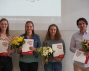 Vier Menschen stehen in einer Reihe, jeder hält einen Blumenstrauß und eine Urkunde mit der Aufschrift „Ullrich Hanses Preis 2022“ in den Händen und repräsentiert stolz die Hochschule Coburg. Sie lächeln vor einem weißen Hintergrund, über ihnen ist eine Leinwand.