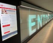 Eine digitale Informationstafel im U-Bahnkorridor informiert über Neuigkeiten und Ankündigungen. Gegenüber ist auf einer beleuchteten Wand teilweise „ENTDECKEN“ zu sehen, eine Einladung zum Entdecken. Dieser moderne, schlichte Raum spiegelt auf subtile Weise die Innovationskraft der Hochschule Coburg wider.