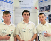 Drei junge Männer in weißen Hemden stehen stolz vor einer Posterpräsentation an der Hochschule Coburg. Sie halten Objekte in den Händen, die mit ihrem Projekt in Zusammenhang stehen, und tragen Namensschilder. Im Hintergrund sind Forschungsmaterial und lebendige Bilder zu sehen, die ihr Engagement und ihre Kreativität widerspiegeln.
