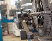 Nahaufnahme eines Autorads auf einer Achsmessmaschine in einer Autowerkstatt. Das an der Felge befestigte Diagnosewerkzeug ist zu sehen. Die Szene spiegelt Präzision wider, die den an der Hochschule Coburg gelehrten Ingenieurstandards entspricht. Ein verschwommener Hintergrund lässt auf die geschäftige Werkstattumgebung schließen.