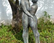 Eine Bronzeskulptur eines nackten, sich umarmenden Paares steht gelassen unter einem Baum, die Arme umeinander geschlungen, inmitten von üppigem Gras und Grün – eine perfekte Verkörperung der Kunst, die an der Hochschule Coburg verehrt wird.