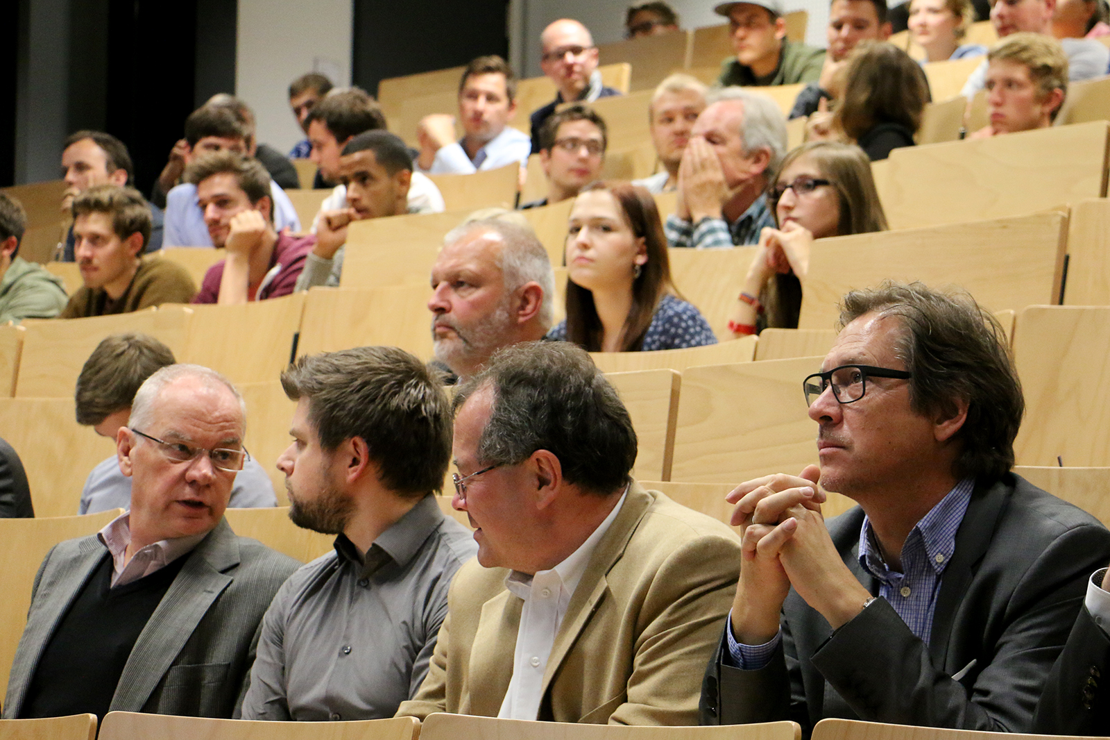 Eine bunt gemischte Gruppe sitzt in einem Hörsaal der Hochschule Coburg. Die Teilnehmer sind engagiert, manche tauschen Gedanken aus, andere konzentrieren sich auf die Präsentation, alles deutet darauf hin, dass es sich um eine akademische oder berufliche Veranstaltung handelt.