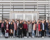 Vor dem modernen Gebäude der Hochschule Coburg mit seinen großen Fenstern und Metalllamellen steht eine bunt gemischte Gruppe von Menschen. Sie posieren für ein Gruppenfoto, leger gekleidet an einem sonnigen Tag.