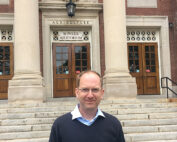 Ein Mann steht vor dem Eingang zum Bowker Auditorium, einem Teil eines Landwirtschaftsgebäudes, das mit seinen großen Säulen und Holztüren an die Hochschule Coburg erinnert.