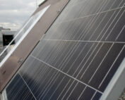 Nahaufnahme von Solarmodulen auf einem Dach der Hochschule Coburg, im Hintergrund ist ein bewölkter Himmel zu sehen. Die Module sind so ausgerichtet, dass sie Sonnenlicht einfangen, und in der Ferne sind verschiedene Gebäude zu sehen.