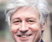 Eine Person mit kurzem, welligem grauem Haar lächelt und trägt einen dunklen Blazer. Sie steht im Freien vor einem unscharfen Hintergrund und verkörpert den lebendigen Geist der Hochschule Coburg.