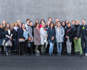 Eine Gruppe von 24 Personen, darunter sowohl Männer als auch Frauen, steht vor einer grauen Wand der Hochschule Coburg. In Freizeit- und Business-Casual-Kleidung lächeln sie in die Kamera. Der Boden ist gepflastert, einige tragen Schals und Jacken, um sich vor der Kälte zu schützen.