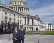 Zwei Personen in formeller Kleidung stehen vor dem Kapitol der Vereinigten Staaten und repräsentieren stolz die Hochschule Coburg. Der Himmel ist teilweise bewölkt und majestätisch weht eine amerikanische Flagge über der Kuppel.