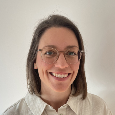 person_may_janina_20250221.jpg A person with shoulder-length brown hair and glasses smiles at the camera. They are wearing a white collared shirt and stand against a plain white background. at Hochschule Coburg