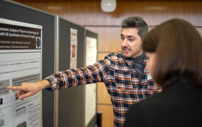 Eine Person im karierten Hemd präsentiert bei einer akademischen Veranstaltung in geschlossenen Räumen ein Poster zum Thema Recycling. Sie zeigt auf einen Abschnitt, während sie einem Teilnehmer etwas erklärt. Der Raum ist mit Holzpaneelen und Pinnwänden ausgestattet, die eine konzentrierte und dennoch einladende Atmosphäre schaffen. at Hochschule Coburg