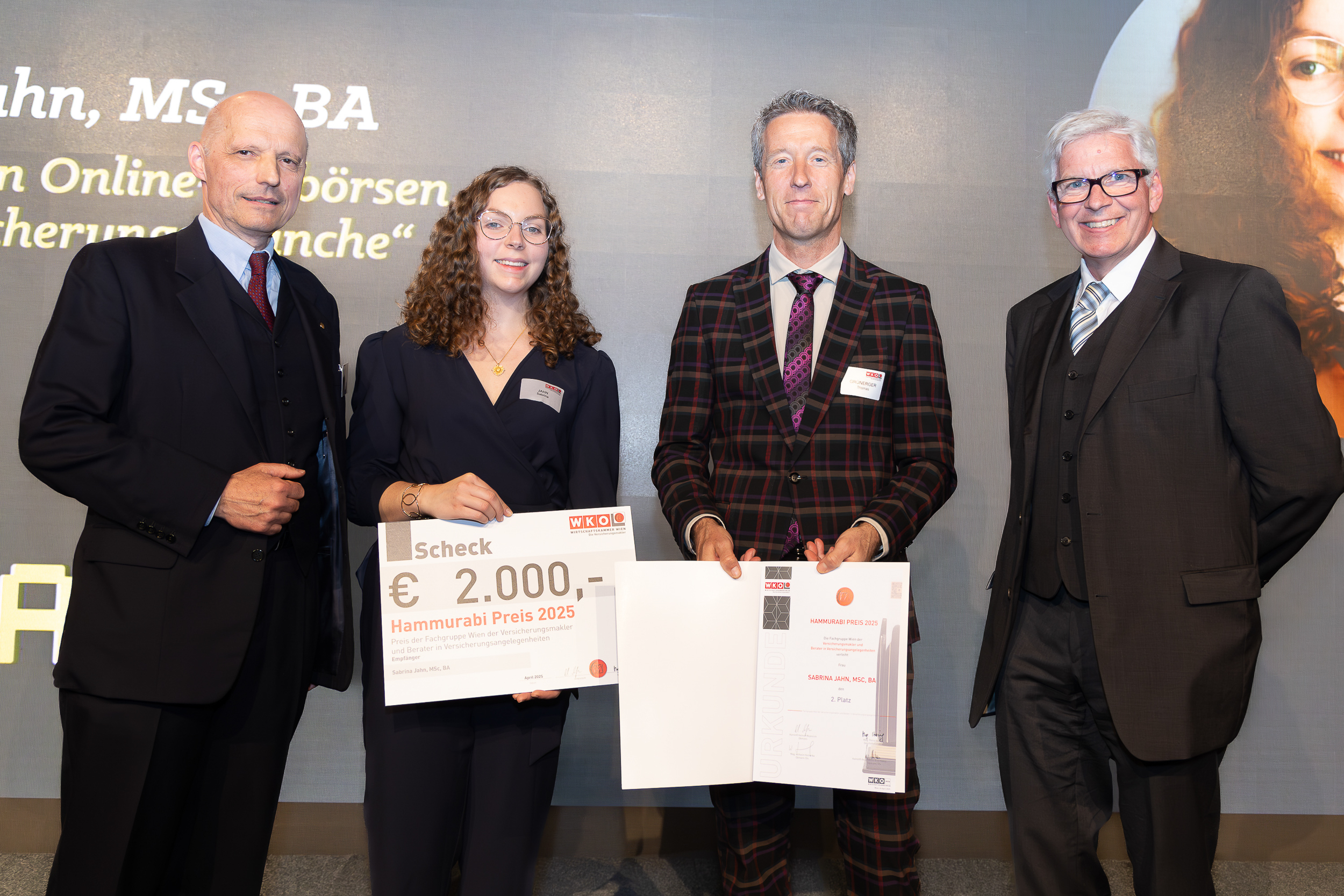 Vier professionell gekleidete Menschen stehen bei einer Preisverleihung in Wien zusammen. Eine Coburger Studentin hält einen großen Scheck über 2.000 Euro mit der Aufschrift „Hammurabi Preis 2025“ in den Händen. Die Gruppe lächelt in die Kamera. at Hochschule Coburg