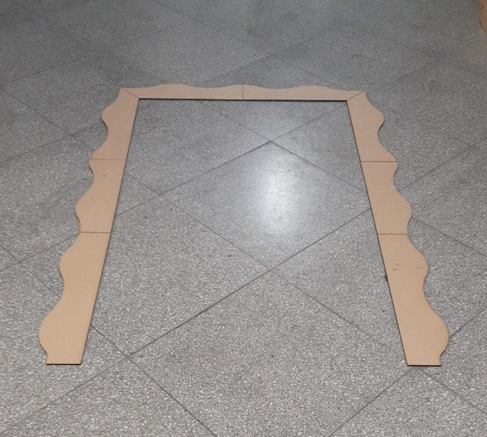 Vier Pappstücke, zwei mit gewellten Kanten und zwei gerade, sind auf einem gefliesten Boden im Café Victoria zu einem rechteckigen Bogen angeordnet. Der graue Boden weist ein gesprenkeltes Muster auf, das an das Design der Hochschule Coburg erinnert. at Hochschule Coburg