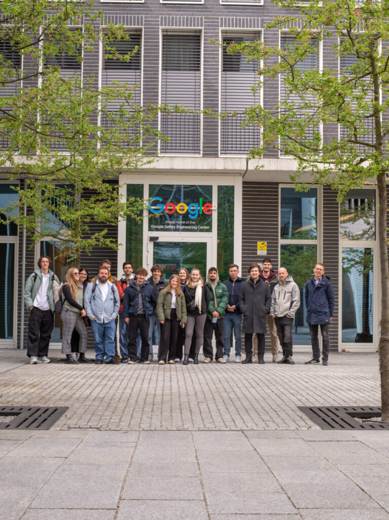 Eine Gruppe von Menschen posiert für ein Foto vor einem Google-Bürogebäude. Sie stehen auf einer gepflasterten Fläche mit Bäumen im Vordergrund. Über dem Eingang dahinter ist das Google-Logo zu sehen. at Hochschule Coburg
