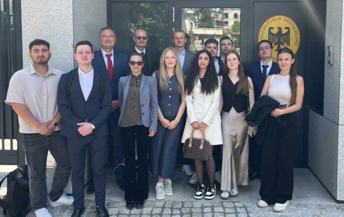 Eine Gruppe von dreizehn Personen in Business- und Freizeitkleidung steht gemeinsam vor einem modernen Gebäude mit Steinmauern und einem Schild mit der Aufschrift „Deutsch-Bulgarisches Studien-Projekt“ vor der Tür des deutschen Konsulats bzw. der Botschaft. at Hochschule Coburg