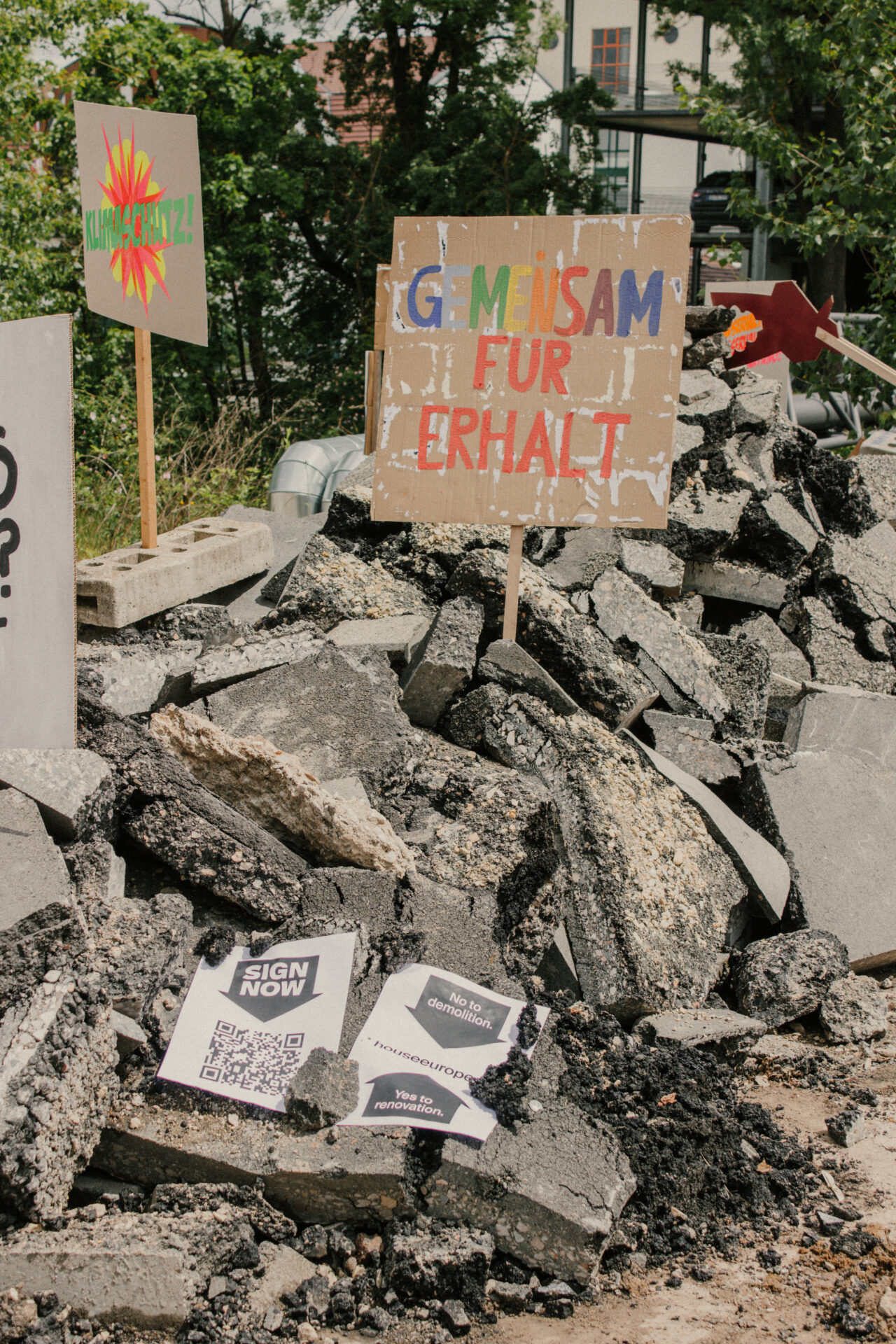 Auf dem INSIDE CAMPUS sind zwischen den Betontrümmern Protestschilder aus Pappe in deutscher Sprache aufgestellt, darunter ein Schild mit der Aufschrift „Gemeinsam für Erhalt“. Auch Flyer, QR-Codes und Botschaften von „Zukunft gestalten“ sind auf den Trümmern verstreut. at Hochschule Coburg